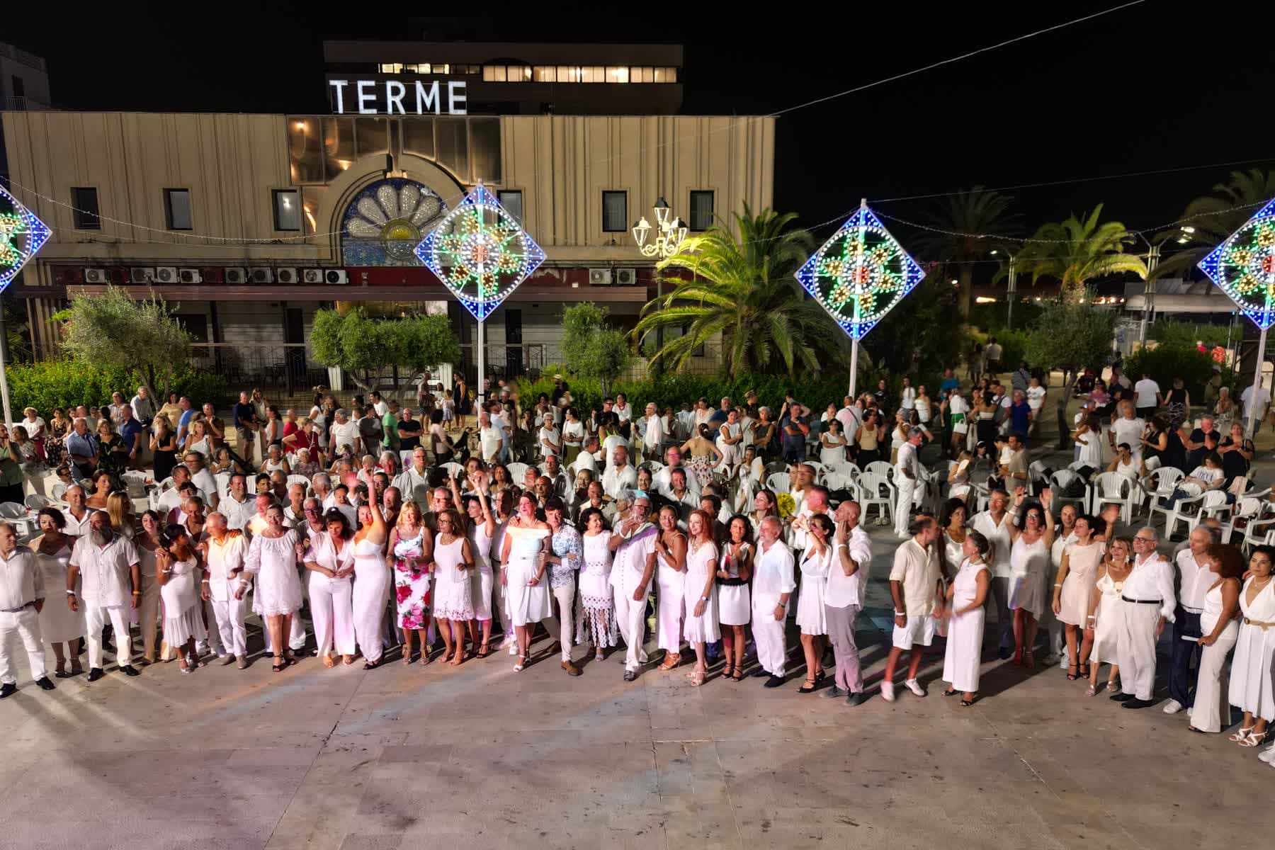 Foto di gruppo dei ballerini vestiti di bianco davanti alle Terme, sotto le luminarie