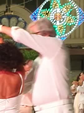 Una coppia in bianco balla sotto le luminarie